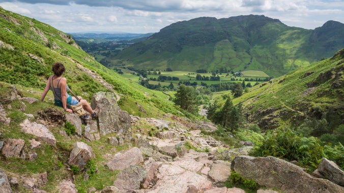 Walker looking down over a green valley with a stream and stone path